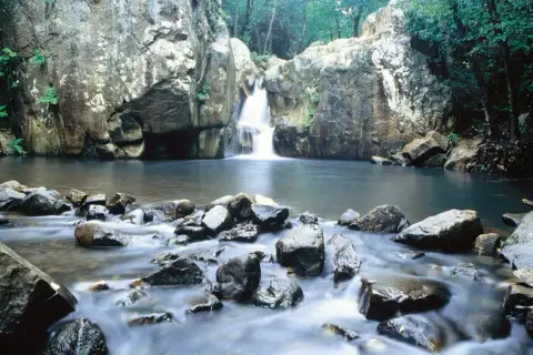 Cascada y río en la ruta del Río de la Miel, rodeado de rocas y vegetación exuberante.