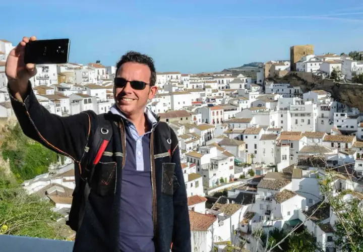Hombre sonriente se toma selfie con el pueblo blanco de Bornos al fondo. ¡Descubre cómo llegar a este pintoresco lugar!