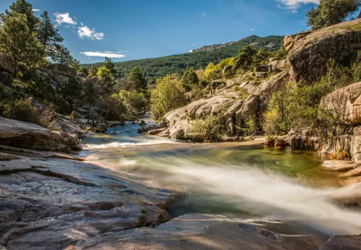 Un río serpentea entre rocas y vegetación, un paisaje idílico para descubrir rutas con encanto cerca de Madrid.