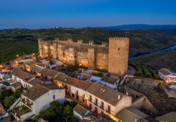 Imponente castillo, posiblemente el castillo más antiguo de España, iluminado al anochecer sobre un pueblo blanco.