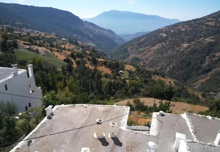 Paisaje montañoso con casas blancas y tejados planos. El camino a Trevélez se abre paso entre verdes colinas y valles profundos bajo un cielo azul.