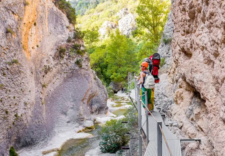 Senderistas disfrutan de las **pasarelas del Vero**, un camino metálico que serpentea por un cañón rocoso con un río cristalino.