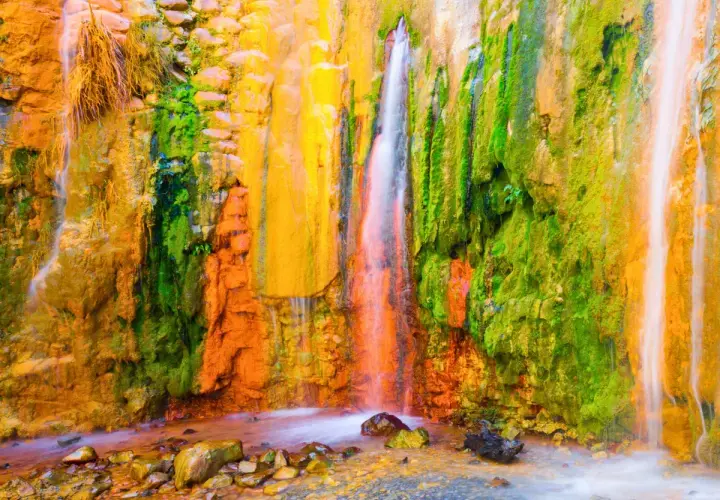 La cascada de los colores, un espectáculo natural con agua cayendo sobre rocas teñidas de vibrantes tonos ocres, verdes y amarillos.