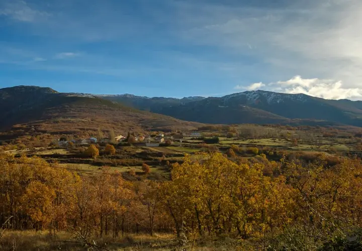 Paisaje otoñal con un pueblo en la ladera. Las montañas nevadas al fondo sugieren la ruta a la laguna negra.