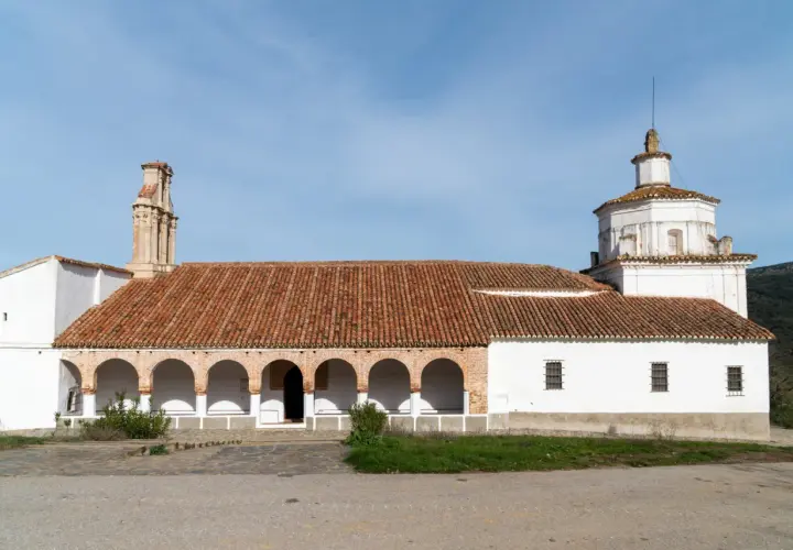 La ermita Virgen del Ara, con su tejado de tejas rojas y arcos blancos, se alza bajo un cielo azul.