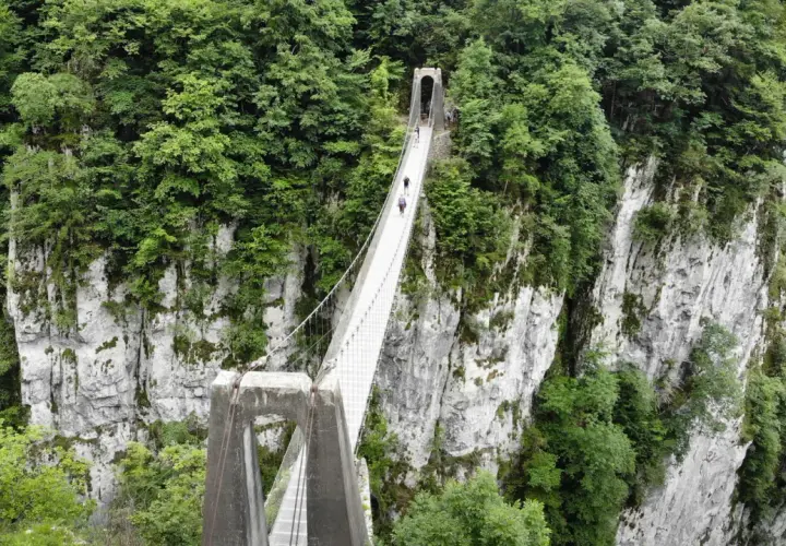 La pasarela de Holtzarte cruza un profundo cañón verde, con personas caminando sobre ella.