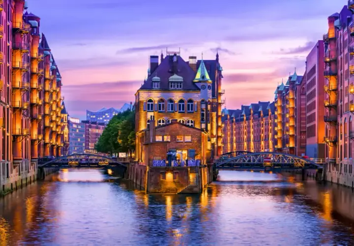 Canal de Hamburgo al atardecer, perfecto para saber donde ir en el puente de diciembre. Edificios de ladrillo iluminados reflejándose en el agua.
