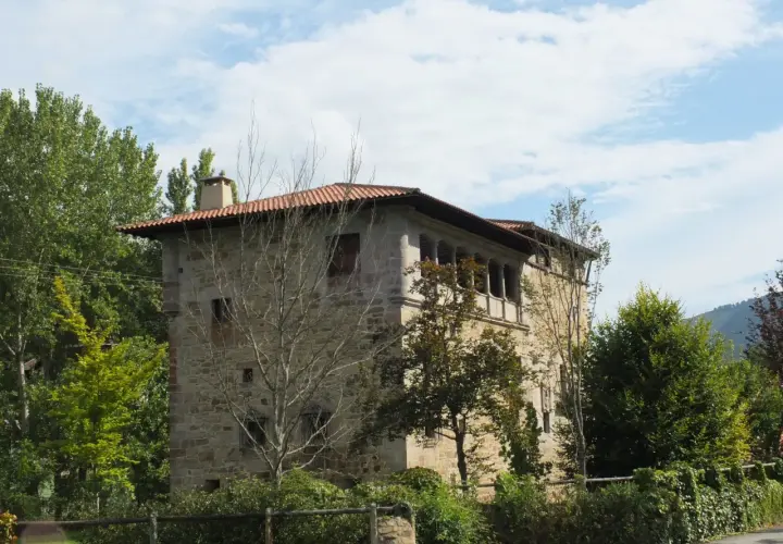 Edificio de piedra con tejado rojo y balcones, rodeado de árboles verdes. Un lugar con encanto, ideal para saber artziniega como llegar.