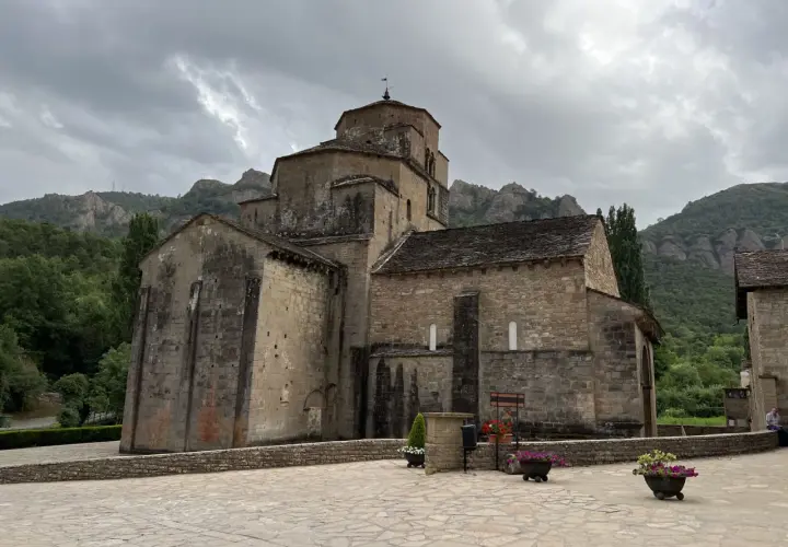 Iglesia románica de piedra con montañas al fondo. Un lugar histórico que evoca la grandeza del puente la reina.