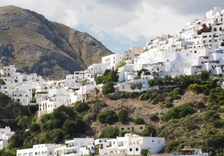 Casas blancas se aferran a una ladera montañosa, un laberinto de calles que invitan a descubrir Mojácar. ¿Cómo llegar? Sigue el sol.
