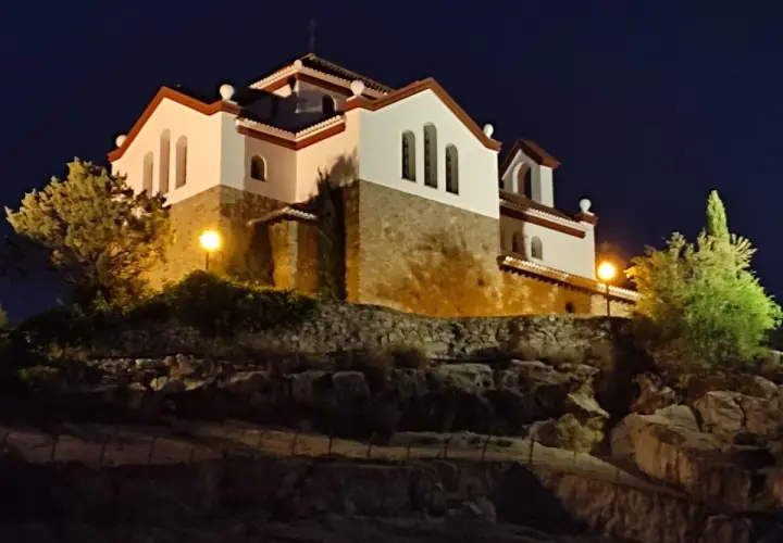 La ermita de los Tres Juanes, iluminada de noche, se alza sobre una colina rocosa.