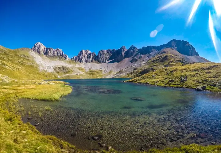 El ibón de Acherito, un lago de montaña de aguas cristalinas, rodeado de prados verdes y picos rocosos bajo un cielo azul intenso.