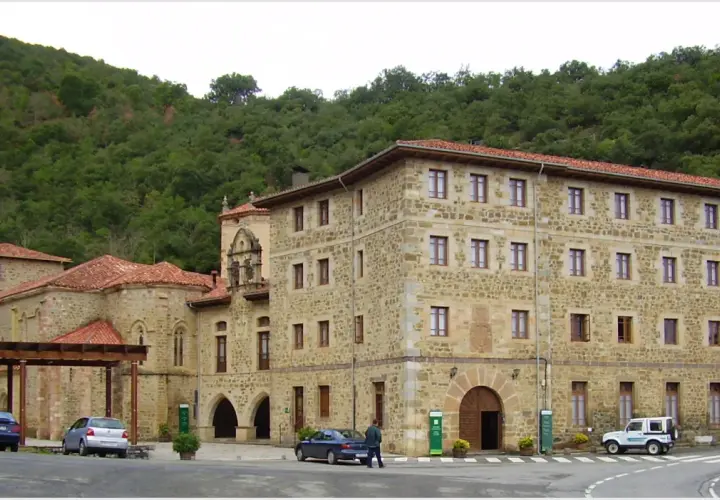 Edificio de piedra con tejados rojos, parte del monasterio de Santo Toribio de Liébana, rodeado de vegetación.