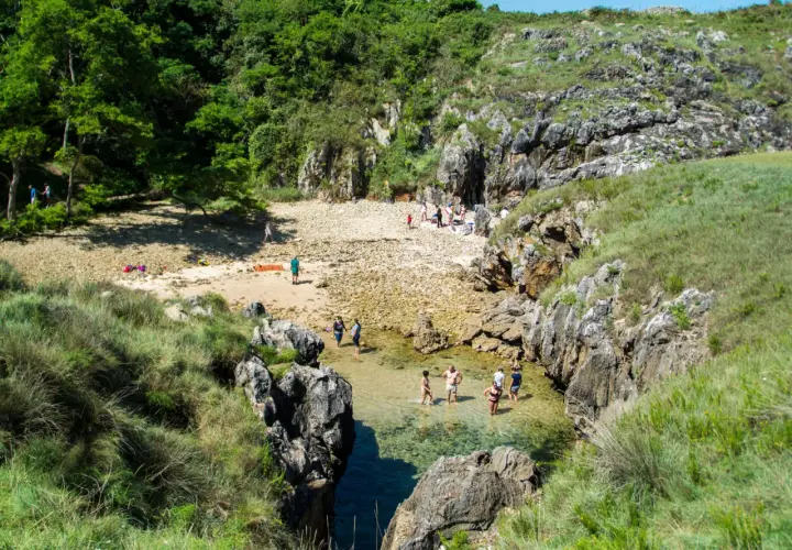 Gente disfrutando del sol y el agua cristalina en la playa de cobijero, rodeada de rocas y vegetación exuberante.