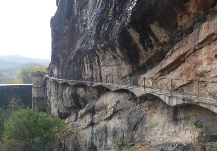 Un pontón de la oliva se aferra a un acantilado rocoso, con un camino bordeado de barandillas que serpentea a lo largo.
