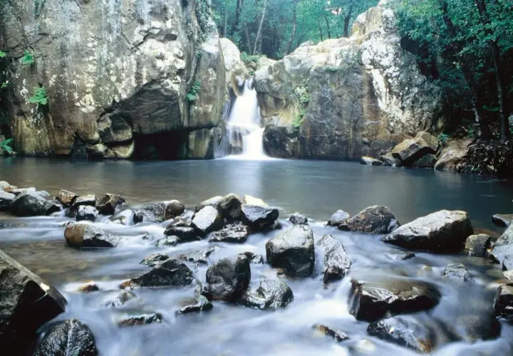 Cascada y río en la ruta del Río de la Miel, rodeado de rocas y vegetación exuberante.