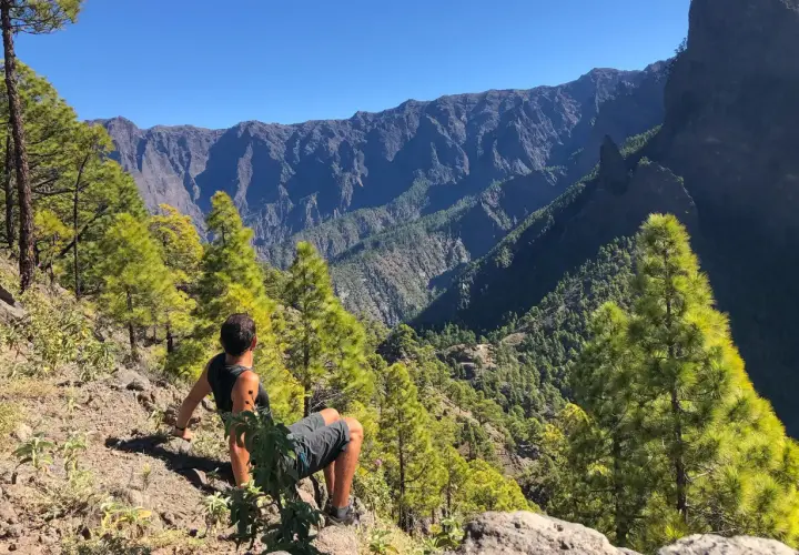 Hombre sentado en la ladera, contemplando el imponente paisaje montañoso del **cubo de la galga**.