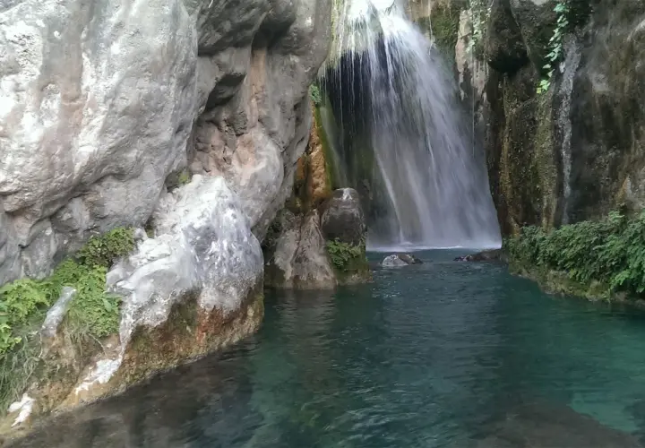 Cascada en las fuentes del Algar, con aguas turquesas y vegetación exuberante entre rocas.