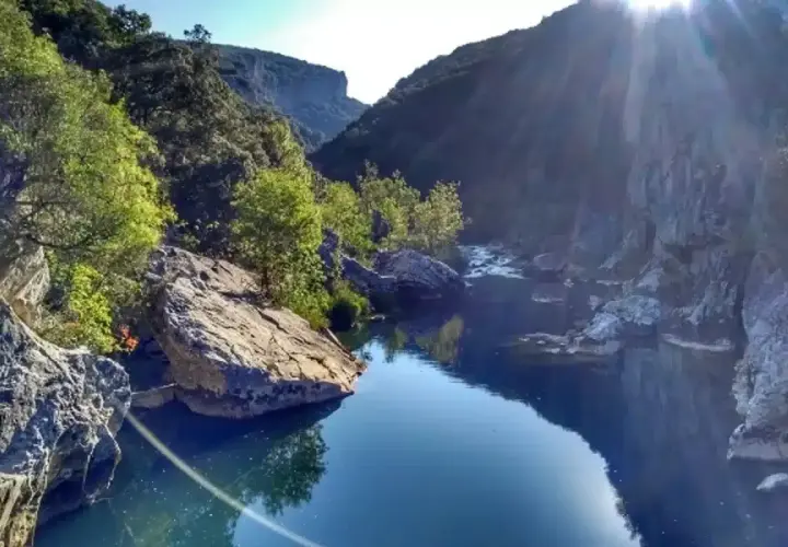 Río sereno en la Foz de Lumbier, un paisaje ideal para una ruta. Rocas y vegetación bordean el agua azul bajo el sol.