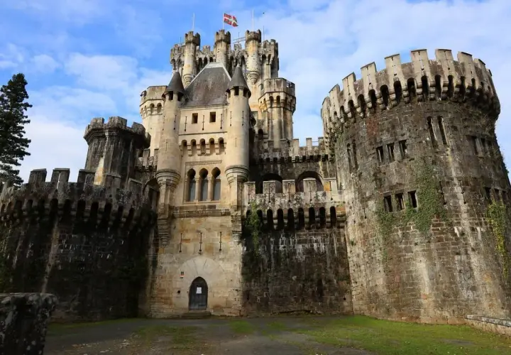 El imponente castillo de Butrón, con sus torres y murallas de piedra, se alza majestuoso bajo un cielo azul con nubes.
