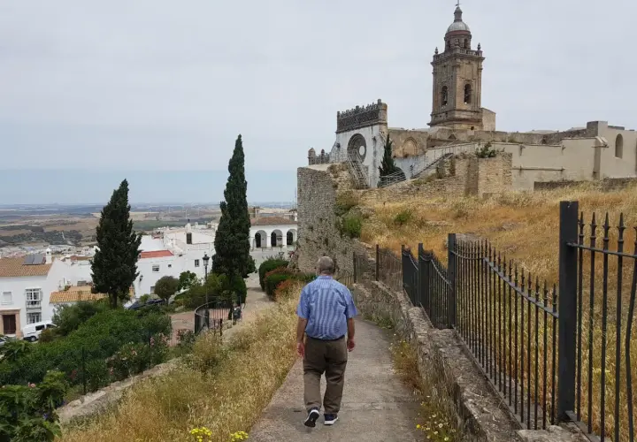 Hombre camina por sendero hacia iglesia en Medina Sidonia. Descubre cómo llegar a este pueblo blanco andaluz.