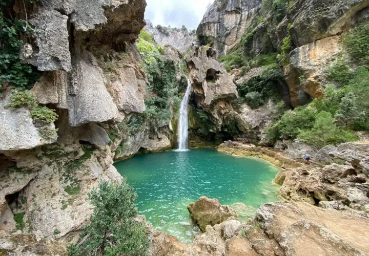 La cascada de la calavera cae en una poza de agua turquesa, rodeada de rocas y vegetación exuberante.