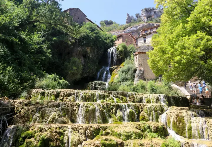 Cascada en las Hoces del Ebro, con casas de piedra integradas en la roca y vegetación exuberante.