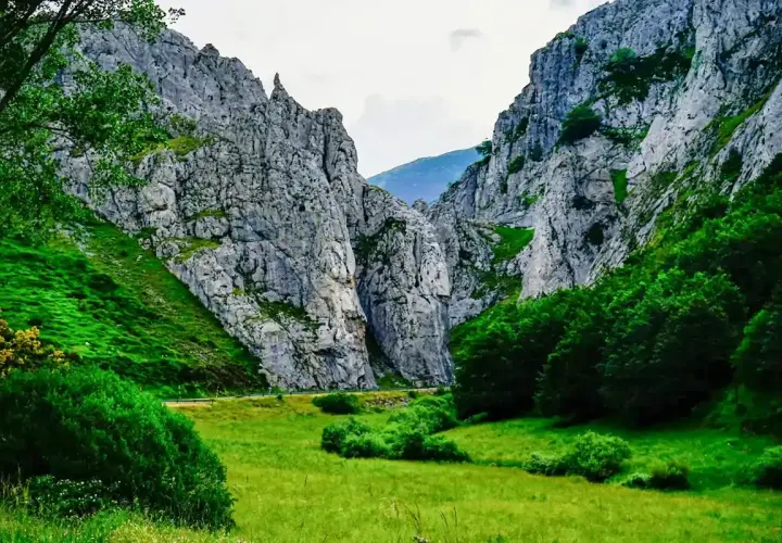 Majestuosas rocas flanquean un valle verde, donde la **cascada de Mazobre** se esconde entre la vegetación exuberante.