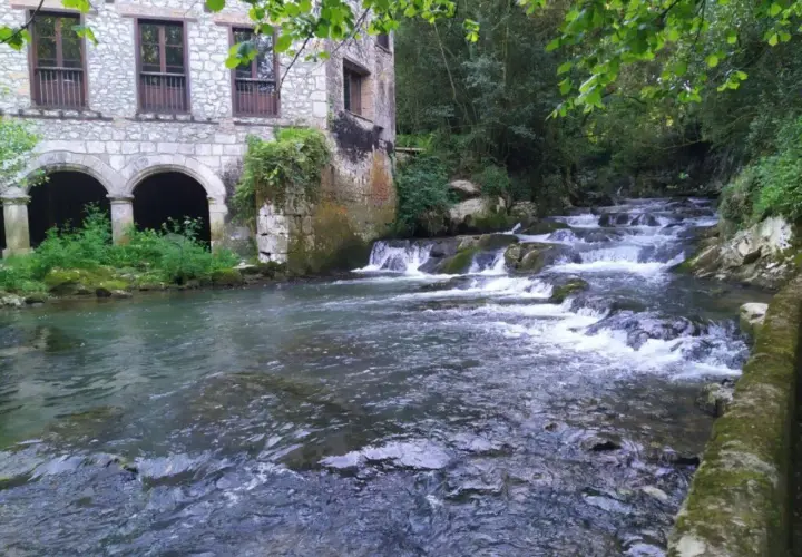 Edificio de piedra con arcos junto a un río con cascadas. Parece la fuente del francés, un lugar idílico.