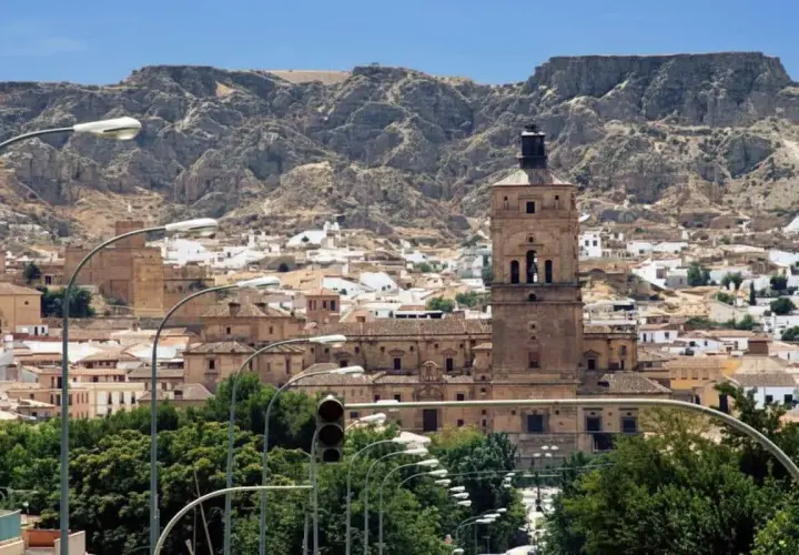 Vista panorámica de Guadix, con su imponente torre campanario y casas blancas al pie de montañas rocosas. Ideal para planificar cómo llegar.