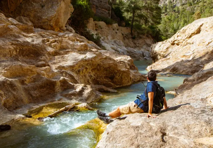 Hombre sentado junto a un río turquesa en un cañón rocoso. Un lugar idílico para explorar, ¡así es como llegar!