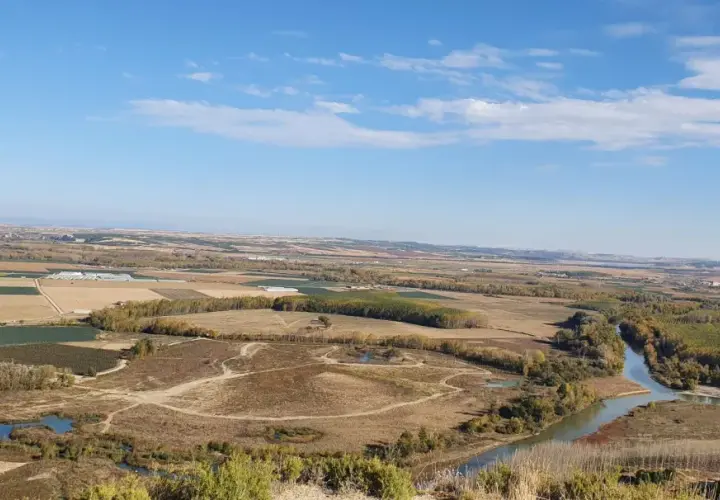 Paisaje rural con un río serpenteante cerca de Villafranca del Bierzo. Campos cultivados y árboles de otoño bajo un cielo azul con nubes.