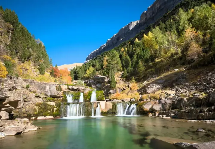 Cascada en un valle montañoso con árboles otoñales, ideal para las mejores rutas senderismo España.