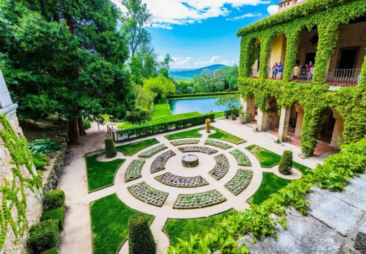 Jardín renacentista con estanque y edificio cubierto de hiedra, evocando la serenidad de los Cuacos de Yuste.
