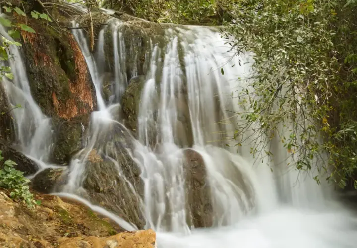 Cascadas de Hueznar, un velo de agua blanca desciende por rocas cubiertas de musgo y vegetación exuberante.