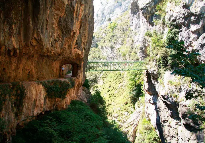 Un puente verde cruza un desfiladero rocoso, parte de la ruta del Cares. El tiempo parece perfecto para esta aventura.