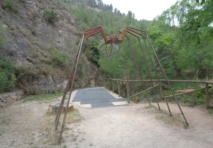 Escultura de araña gigante en la ruta de las esculturas Bogarra, con un cuerpo de alambre y patas metálicas, sobre un camino de grava.