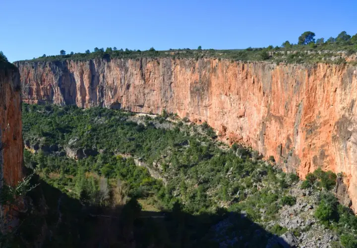 Impresionante cañón con paredes rojizas y vegetación verde. Los puentes colgantes de Chulilla se asoman entre la naturaleza.