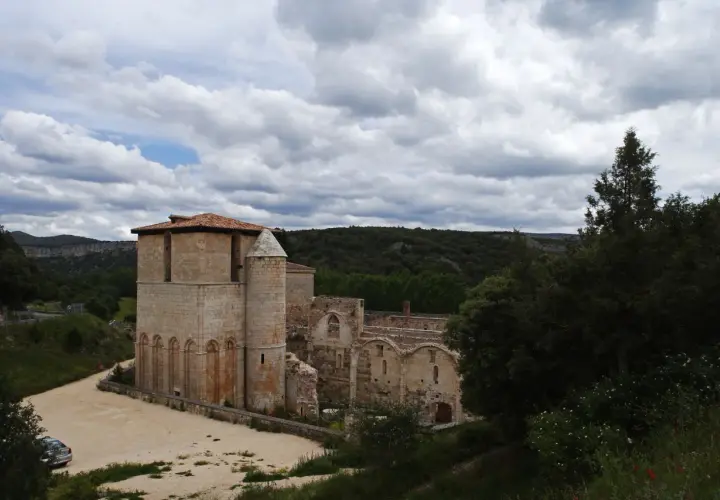 Ruinas del monasterio de San Pedro de Arlanza, con su torre robusta y arcos de piedra bajo un cielo nublado.