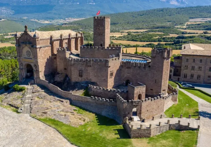 Imponente castillo de Javier, con su basílica anexa y torres defensivas, se alza majestuoso sobre un paisaje verde y montañoso.