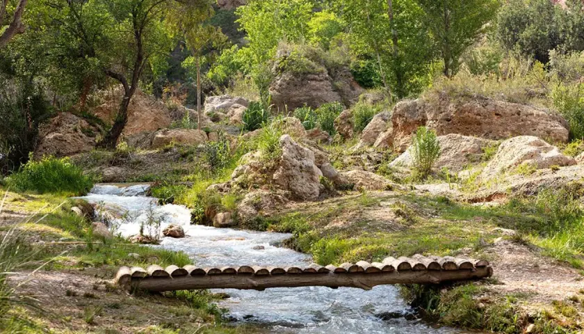 Un puente rústico cruza un arroyo en un paisaje rocoso y verde. Descubre cómo llegar a este rincón natural.