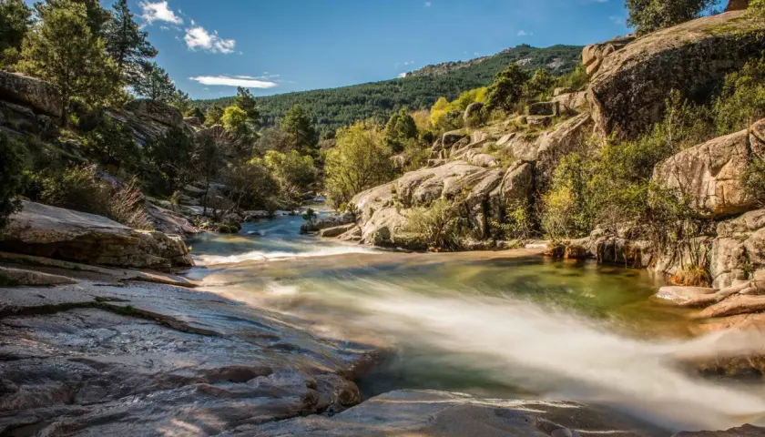 Un río serpentea entre rocas y vegetación, un paisaje idílico para descubrir rutas con encanto cerca de Madrid.