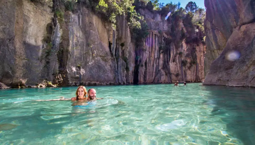 Pareja sonriente nada en las aguas cristalinas de la fuente de los baños de Montanejos, rodeados de imponentes acantilados.