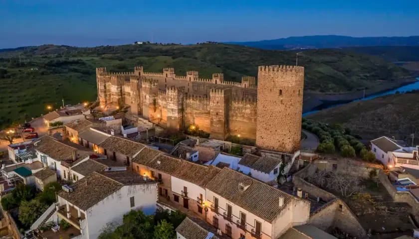Imponente castillo, posiblemente el castillo más antiguo de España, iluminado al anochecer sobre un pueblo blanco.