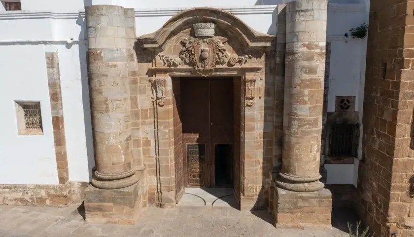Impresionante portal de piedra con detalles ornamentales, flanqueado por columnas. Parece la entrada a una capilla Sixtina extremeña, invitando a descubrir su interior.