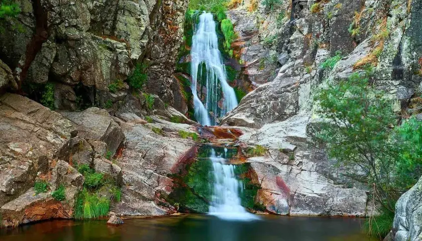 Cascada del Purgatorio, una joya natural en la ruta. Agua cayendo entre rocas y vegetación exuberante.