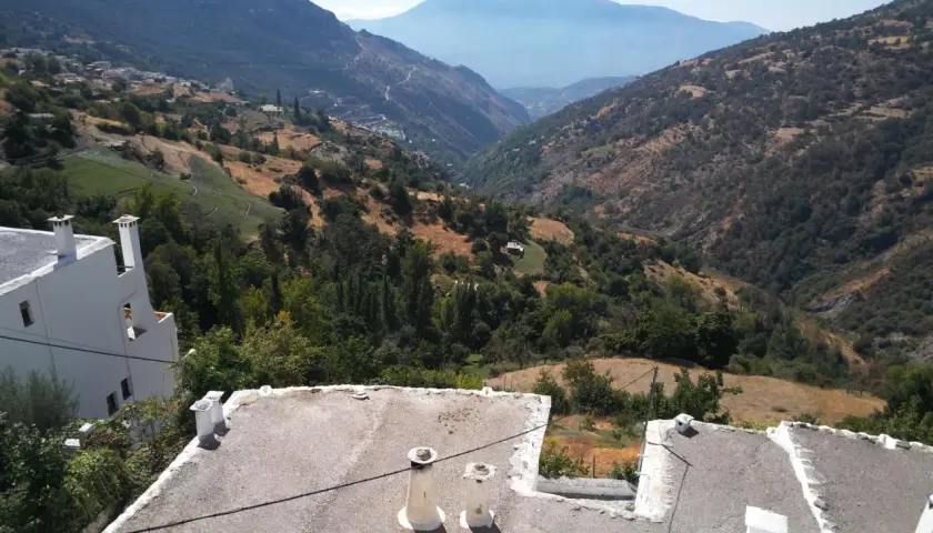 Paisaje montañoso con casas blancas y tejados planos. El camino a Trevélez se abre paso entre verdes colinas y valles profundos bajo un cielo azul.