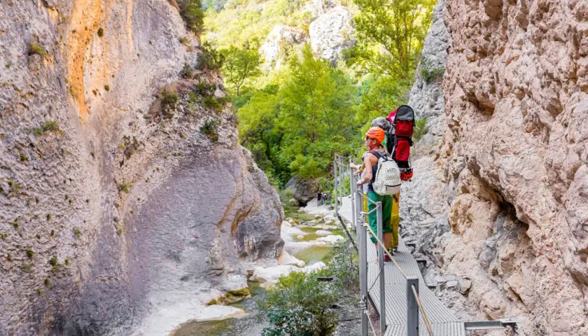 Senderistas disfrutan de las **pasarelas del Vero**, un camino metálico que serpentea por un cañón rocoso con un río cristalino.