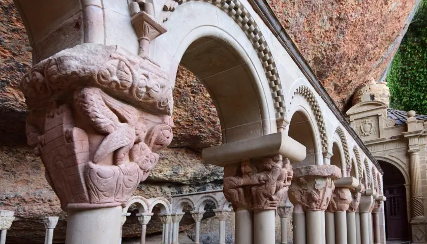 Detalles arquitectónicos y escultóricos en piedra de San Juan de la Peña, con arcos y capiteles tallados bajo una roca.