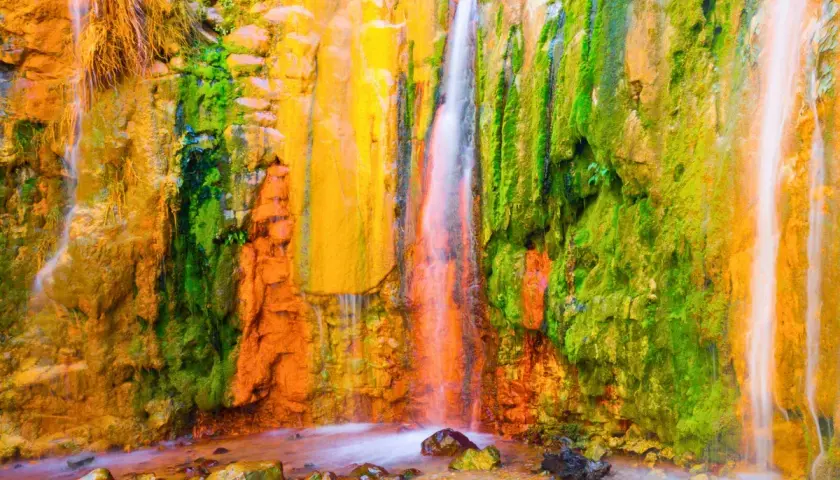 La cascada de los colores, un espectáculo natural con agua cayendo sobre rocas teñidas de vibrantes tonos ocres, verdes y amarillos.